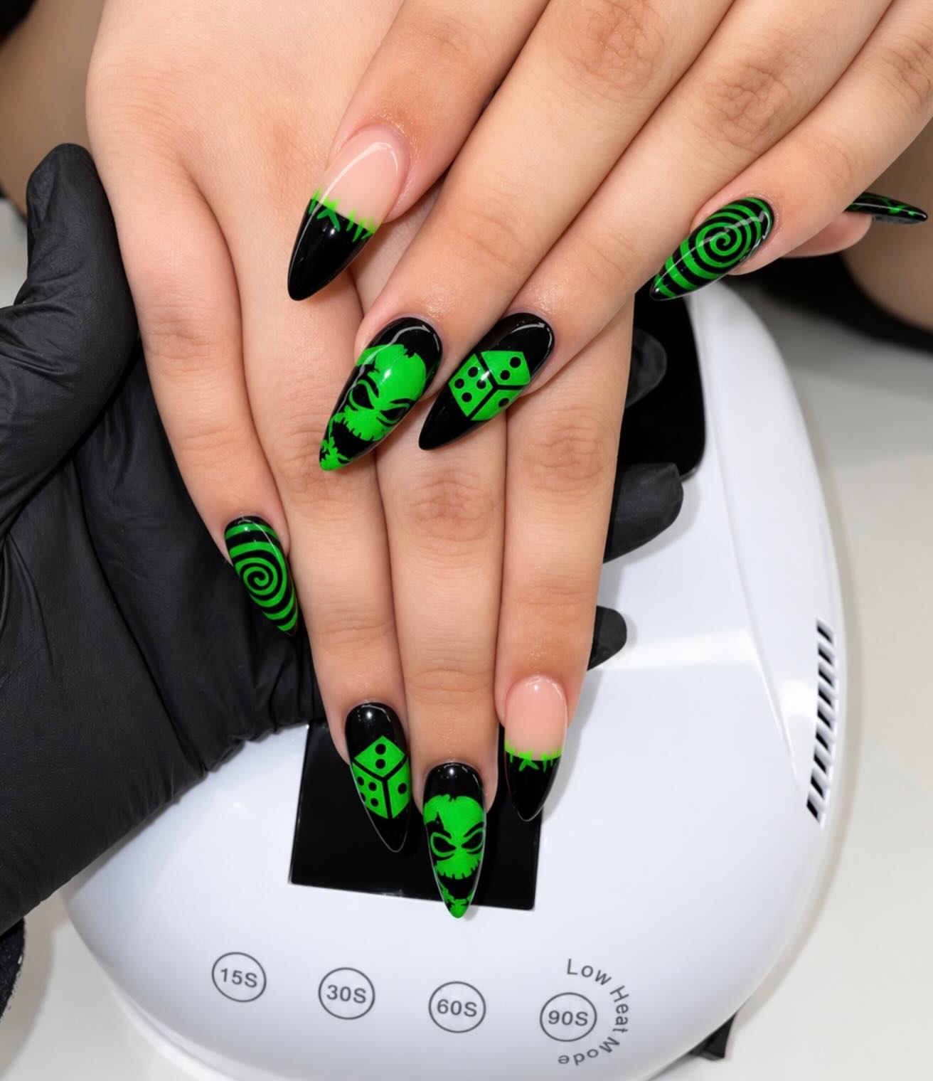 Black almond nails with neon green dice and swirl art under the nail lamp